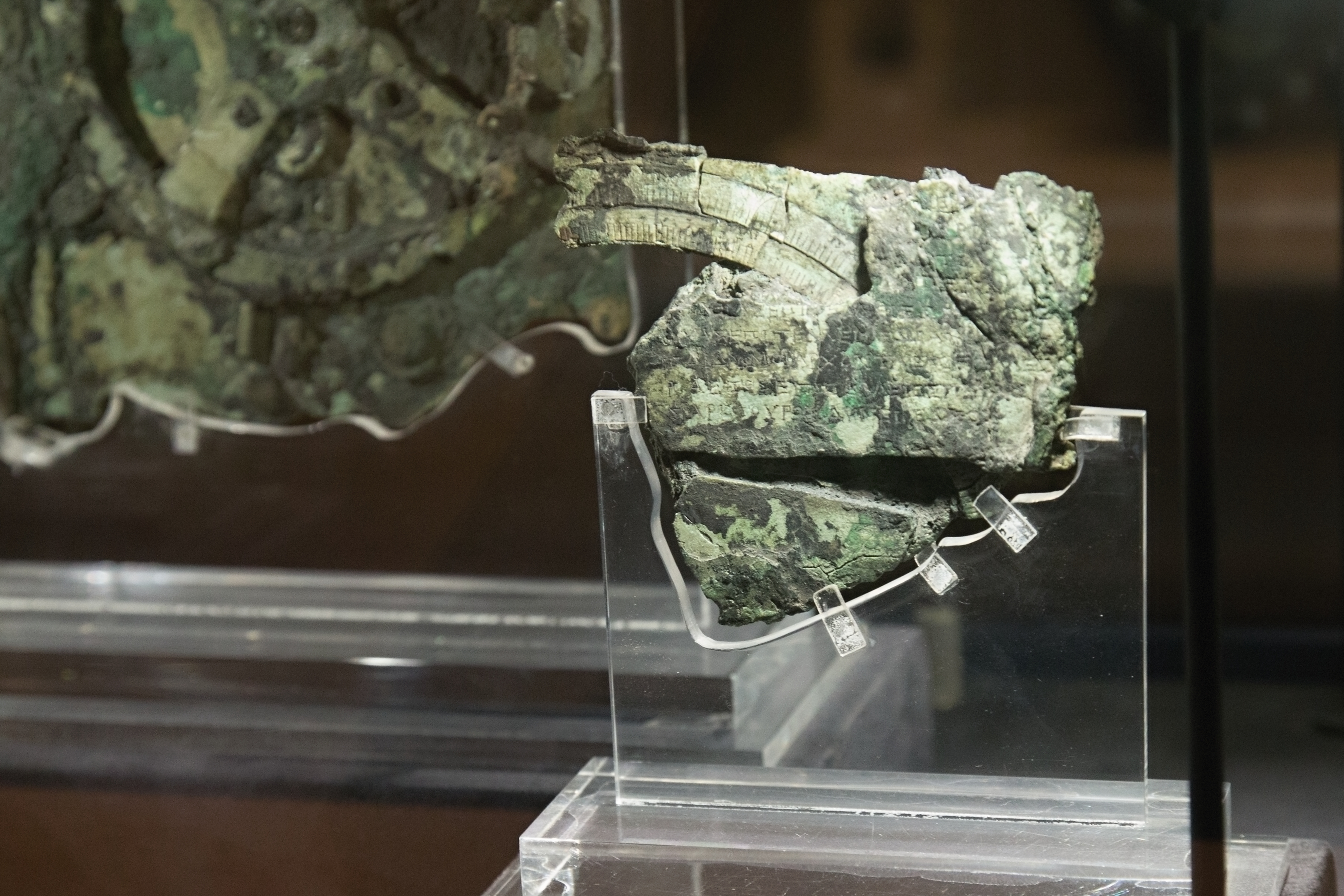 Detail of Antikythera mechanism bronze fragment with visible gear teeth and corrosion.